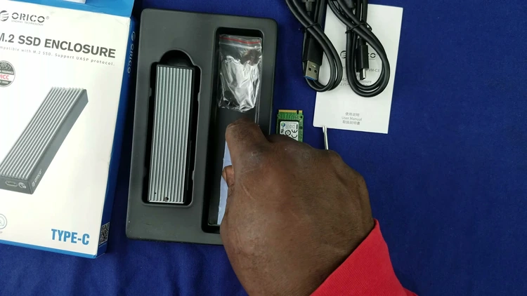 Unboxed contents of the Orico M.2 NVMe SSD enclosure, including the aluminum case, screws, thermal pad, screwdriver, USB-C to C and USB-C to A cables, and an NVMe SSD ready for installation.